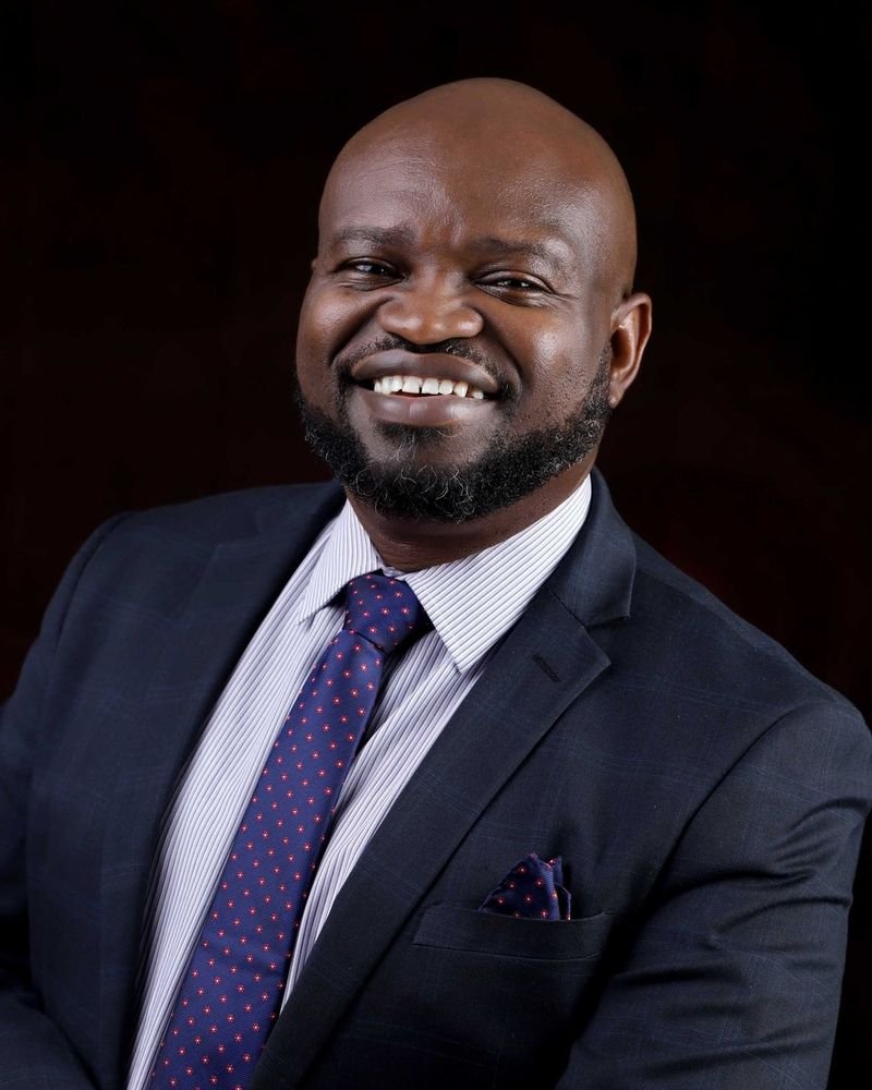 Dr. Ifeanyi Okoye, smiling, in a navy suit and tie